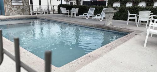 - une piscine avec des chaises blanches, des tables et des chaises dans l'établissement HOTEL LOS ROBLES, à Nuevo Laredo