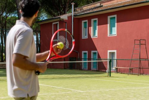 a man holding a tennis ball and racket on a tennis court at Hotel Villa dei Pini in San Terenziano