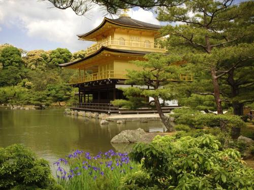 a building in a garden with a pond and purple flowers at SlowTime Hotel Kyoto in Kyoto