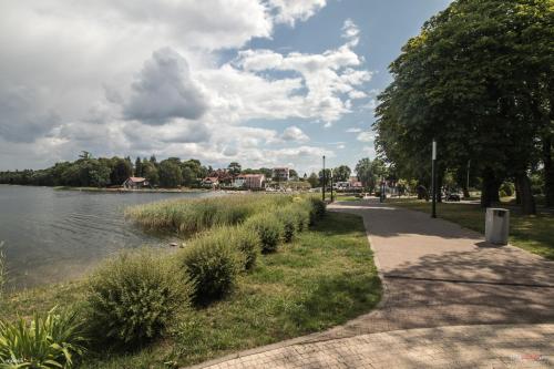 a path next to a river with trees and clouds at Apartamenty Na wzgórzu in Ińsko