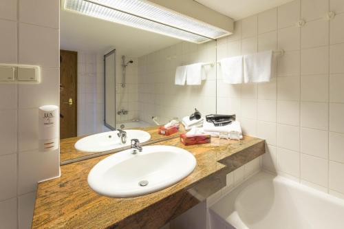 uma casa de banho com 2 lavatórios, uma banheira e um espelho. em Hotel Altdeutsche Weinstuben em Freyburg