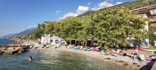 a group of people sitting on a beach near the water at Hotel S.Maria in Brenzone sul Garda