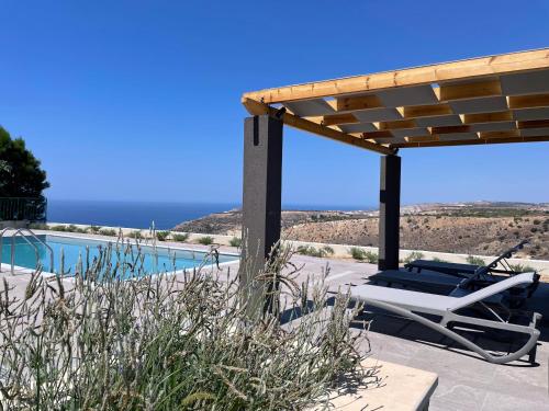 a patio with a pool and a chair under a pergola at Windhill Edge Villa in Pissouri