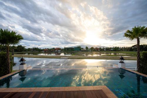 a large swimming pool with palm trees and the sunset at Thantara Resort Chiang Mai in Chiang Mai
