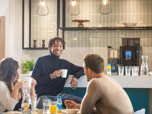 a group of people sitting around a table with a man holding a cup at Aparthotel Adagio London Stratford in London