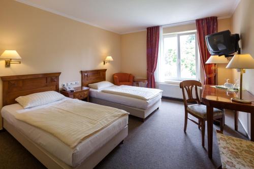 Habitación de hotel con 2 camas, escritorio y TV. en Hotel Garni Schlossgarten, en Neustrelitz
