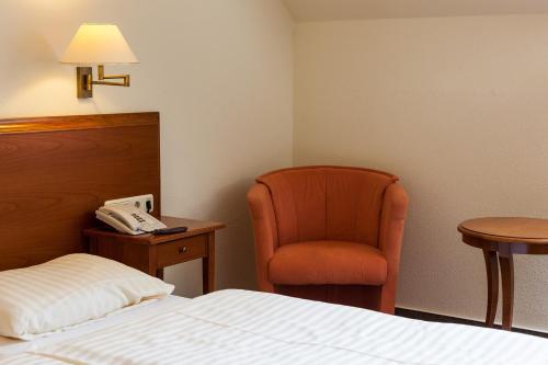 a hotel room with a bed and a chair and a phone at Hotel Garni Schlossgarten in Neustrelitz