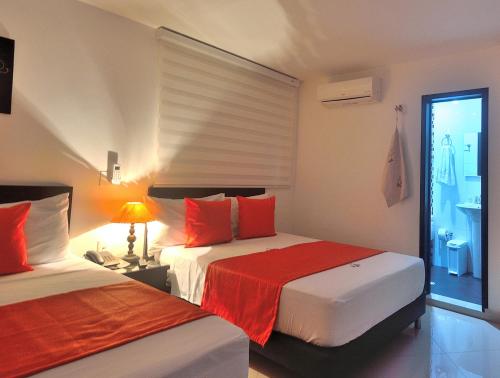a bedroom with two beds with red pillows and a window at La Pera Hotel in Bucaramanga