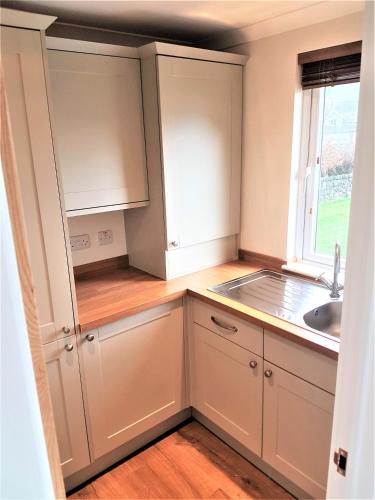 a kitchen with white cabinets and a sink and a window at Llyn Dinas Lodge in Betws-y-coed