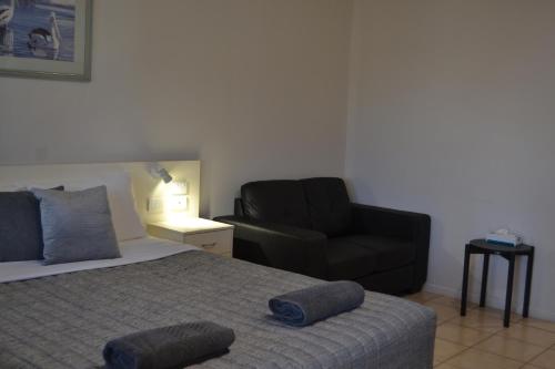 a bedroom with a bed and a black chair at Matilda Motel in Bundaberg