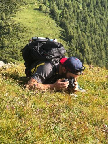 a man with a backpack taking a picture on a hill at Haus Egger in Kartitsch