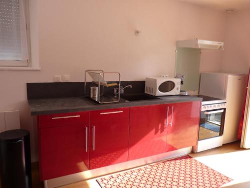 une cuisine avec des armoires rouges et un micro-ondes dans l'établissement Aux Pierres de Nozières, à Gramat