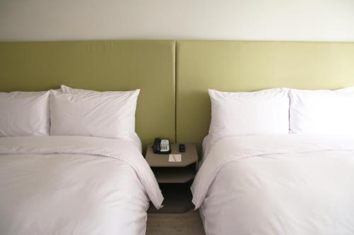 two beds with white sheets and a side table with a clock at Horizon Inn in Taipei