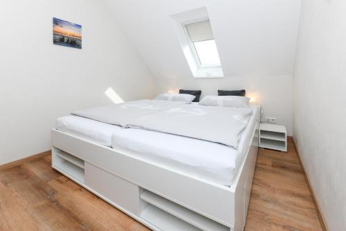 a white bed in a white bedroom with a window at Ferienwohnung im Haus Hafenlicht in Neuharlingersiel