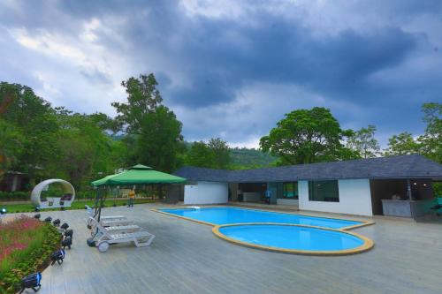a swimming pool with a patio and a building at White Feather Resort Kauncha in Silvassa
