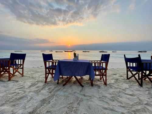 een tafel en stoelen op het strand met zonsondergang bij Zava Nungwi in Nungwi