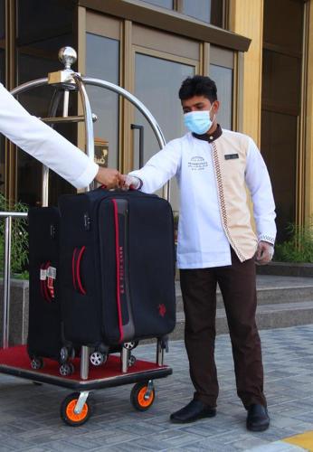 a man in a mask pushing a luggage cart at The Address Palace Apartments in Dammam