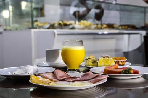 a table with plates of food and a glass of orange juice at Hotel Acalanto in Feira de Santana