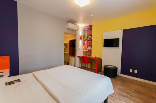 um quarto com uma cama branca e uma parede azul e amarela em Ibis Styles Balneário Camboriú - 1 Quadra do Mar no Balneário Camboriú