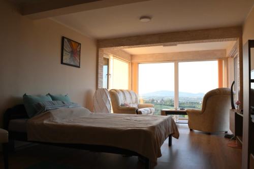 a bedroom with a bed and chairs and a large window at VILA POGLED in Arandjelovac