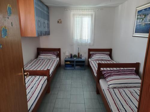 three beds in a room with a window at Apartmani Jakovljevic in Murter