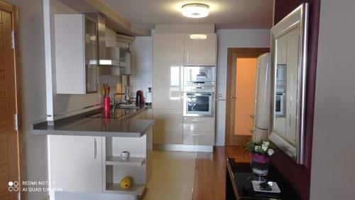 una cocina con armarios blancos y electrodomésticos de acero inoxidable en Apartamento Las Carolinas, en Ribeira