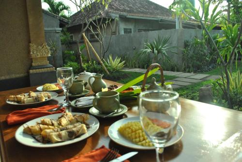 a wooden table with plates of food and wine glasses at Trijaya Guest House Pemuteran in Pemuteran