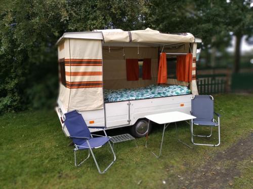 einen Wohnwagen mit zwei Stühlen und einem Bett im Gras in der Unterkunft Retro Vouwwagen in Tynaarlo