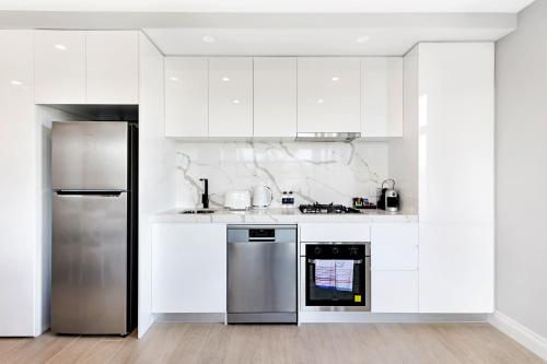 a kitchen with white cabinets and a stainless steel refrigerator at The Hamptons Apartments - St Kilda in Melbourne