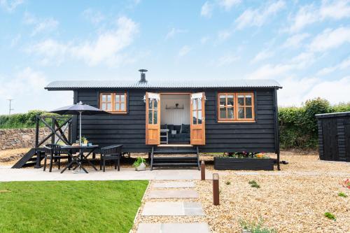 a black tiny house with a table and an umbrella at Daisy Park Shepherds Hut in Looe