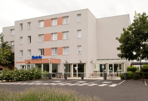 a large white building with a parking lot at Kyriad Clermont-Ferrand-Sud - La Pardieu in Clermont-Ferrand