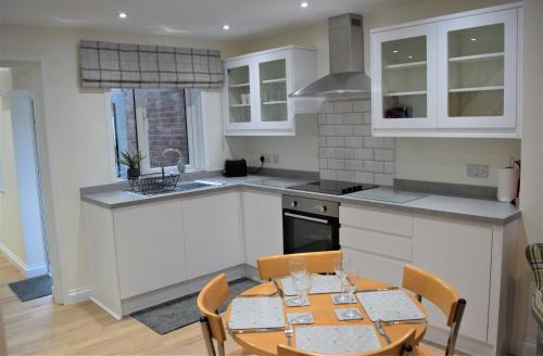 une cuisine avec des placards blancs et une table avec des chaises dans l'établissement Osprey Cottage, Manton in Rutland, à Manton