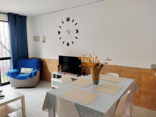 a living room with a table and a clock on the wall at CASA SANTO a 2 minutos de la playa a pié y parking gratuito in Cala del Moral