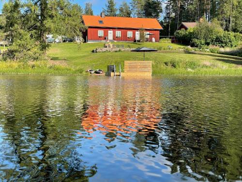 a red house with an umbrella over a lake at Projekt Schwedenalm in Furudal