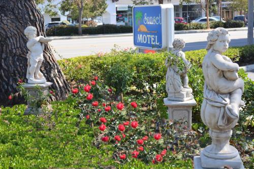 three statues in a garden with flowers and a hotel sign at Sunset Motel in Santa Barbara