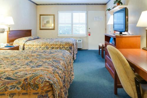 a hotel room with two beds and a desk and a television at Saga Motor Hotel Pasadena in Pasadena
