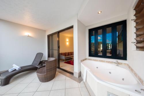 baño con bañera, silla y ventana en at Waterfront Whitsunday Retreat - Adults Only, en Airlie Beach