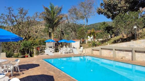 a pool with chairs and umbrellas and a table at Chalés Vila da Serra in Serra Negra