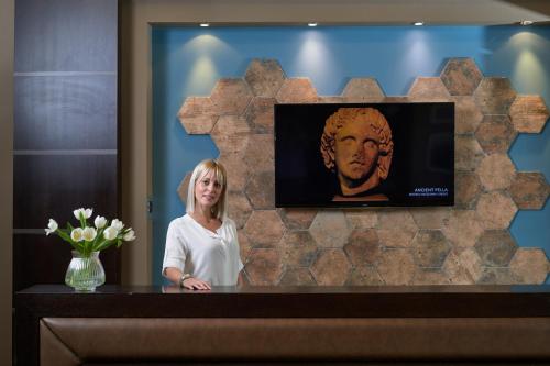 a woman standing behind a counter with a picture of a bust at Maison Hotel in Halkidona
