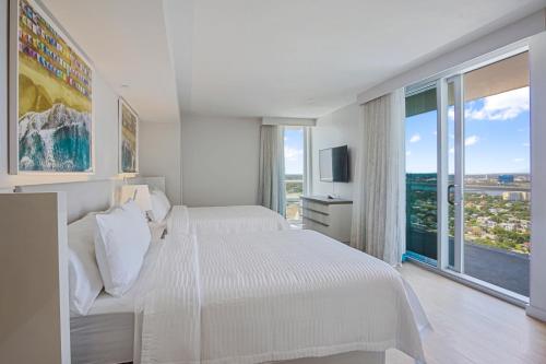 a white bedroom with two beds and a large window at Daytona Grande Oceanfront Resort in Daytona Beach