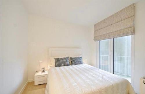 een witte slaapkamer met een bed en een raam bij Luxe appartement Arte, 50m van het Zoute strand in Knokke-Heist