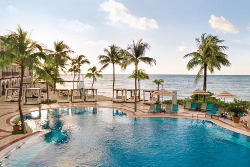 une piscine avec des palmiers et l'océan dans l'établissement Wyndham Alltra Playa del Carmen Adults Only All Inclusive, à Playa del Carmen