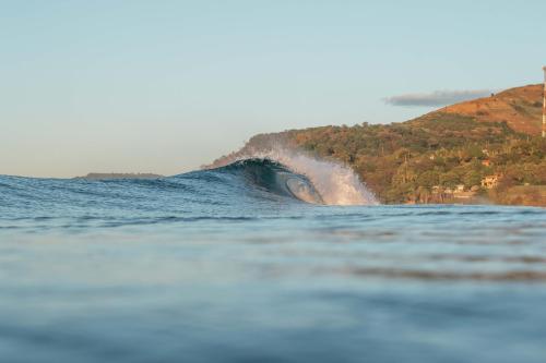 a wave in the ocean with a hill in the background at Esencia Nativa in El Zonte