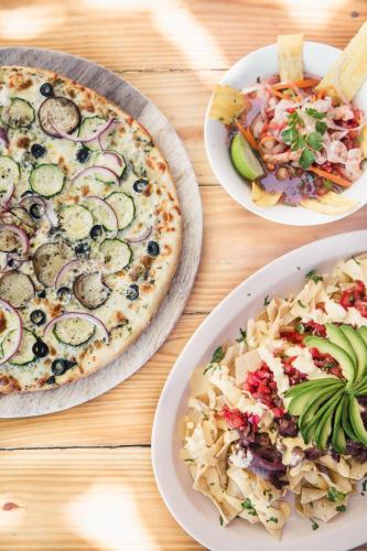 a table with three plates of food and a pizza at Esencia Nativa in El Zonte