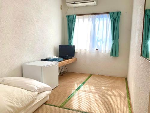 a room with a bed and a television and a window at Pension Sea Friend in Tokashiki