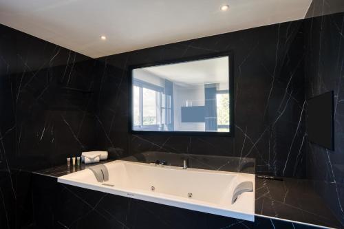 a bath tub in a black bathroom with a mirror at Best Western Plus Le Fairway Hotel & Spa Golf d'Arras in Anzin-Saint-Aubin