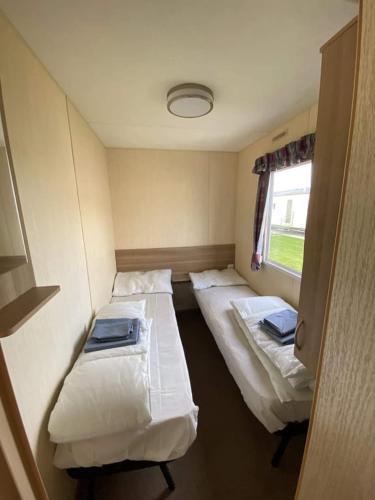 a small room with two beds and a window at 8 BERTH CARAVAN PG30 in Chapel Saint Leonards