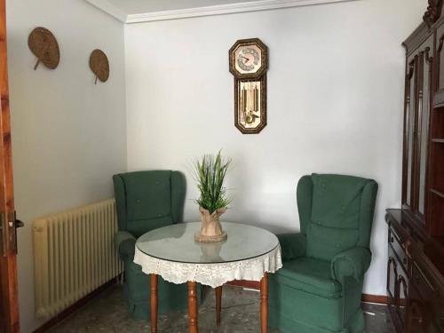 a table and two green chairs and a clock at CASA LATY in La Fregeneda