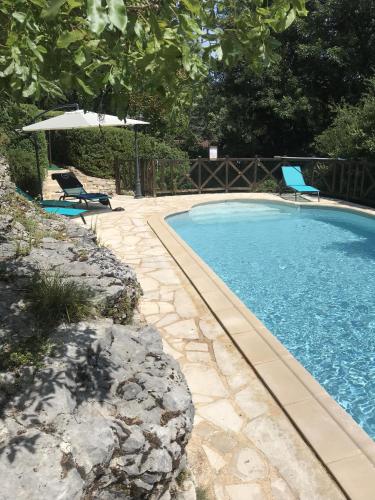 une piscine avec deux chaises et un parasol dans l'établissement Le Mas de Tresse, à Saint-Médard