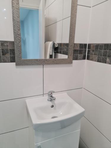 W białej łazience znajduje się umywalka i lustro. w obiekcie Cosy Lodge w mieście Thornton Heath